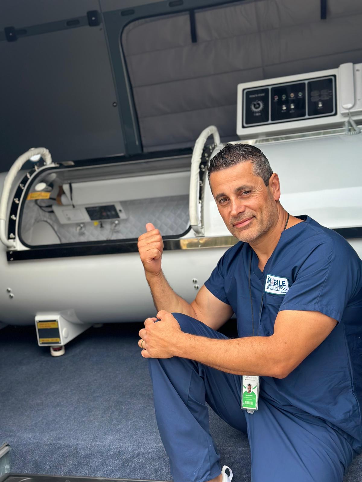 The Mobile Wellness Group team member beside the hard-shell hyperbaric chamber inside the mobile unit